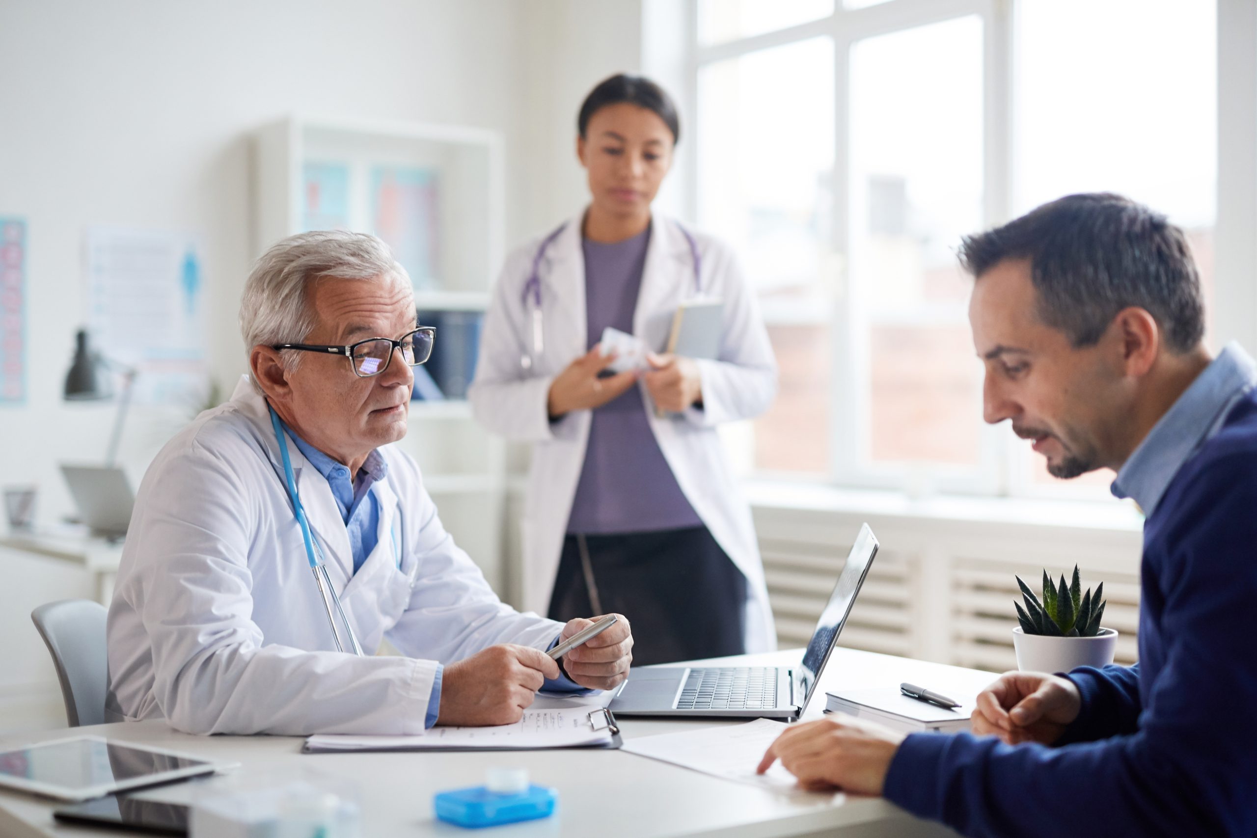 Lekarz rozmawia z pacjentem w gabinecie, jakie badania profilaktyczne dla mężczyzn warto wykonać w poszczególnym wieku, aby cieszyć się zdrowiem i dłuższym życiem.